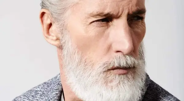 Un homme âgé au regard intense, arborant un modèle de barbe homme blanc et volumineux, avec des cheveux grisonnants coiffés en arrière.