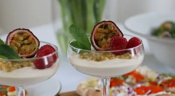 Två glas med len vit chokladmousse, toppade med passionsfrukt, hallon och mynta. En läcker dessert som passar perfekt till fikat.