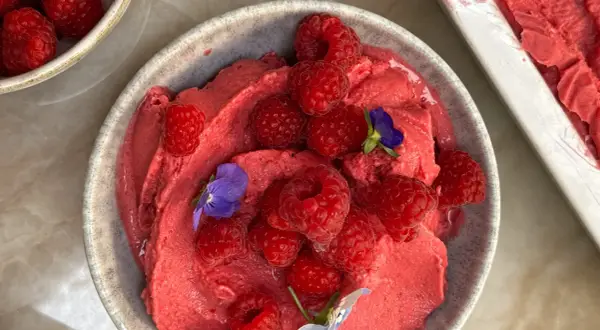 En skål med krämig hallonyoghurtglass toppad med färska hallon och små violer. En härlig sommardessert.