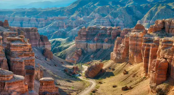Beeindruckende Schluchten und Berge prägen die Kasachstan Landschaft. Ein gewundener Weg führt durch das Tal, umgeben von roten Felsformationen und grünen Hängen.