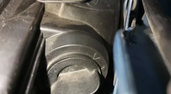 Opel Meriva B wymiana żarówki mijania. Widoczny element mocowania osłony reflektora, przygotowanie do wymiany.