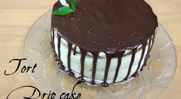 Pyszny tort drip cake z czekoladą spływającą po bokach, ozdobiony różową posypką i listkami.