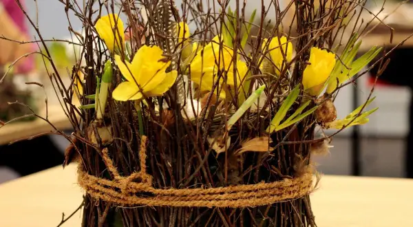 Wielkanocna florystyka na cmentarz: bukiet z żółtych żonkili, gałązek i piór, ozdobiony sznurkiem.