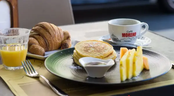 Un délicieux petit déjeuner italien : croissant, pancakes, fruits frais et café. Un régal pour bien commencer la journée !