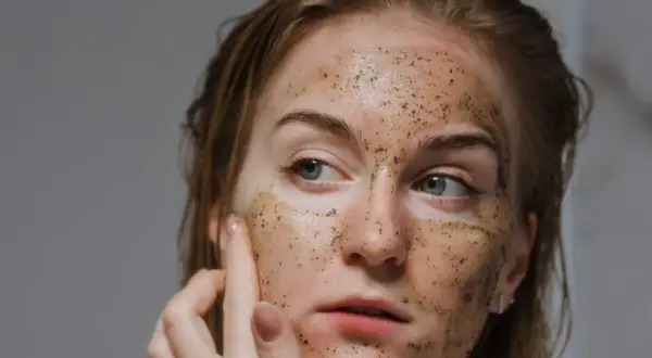 Una donna applica uno scrub viso, scoprendo i benefici di una pelle liscia e luminosa.