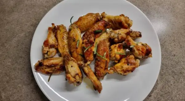 Alette di pollo in padella, dorate e succulente, guarnite con rosmarino fresco. Un piatto invitante pronto per essere gustato.