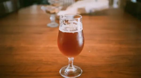 Un bicchiere di birra ambrata su un tavolo di legno. La domanda "quante birre si possono bere al giorno" aleggia nell'aria.