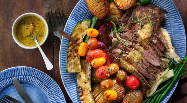 En saftig flankstek, perfekt för att grilla, serveras med grillade grönsaker som zucchini, tomater, potatis och gröna bönor. En härlig måltid!