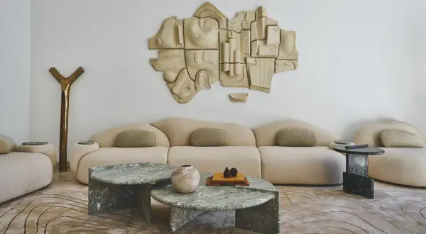 Salon moderne avec canapé beige, tables basses en marbre vert, sculpture murale abstraite et tapis aux motifs organiques. Un endroit parfait pour recevoir une lettre home.