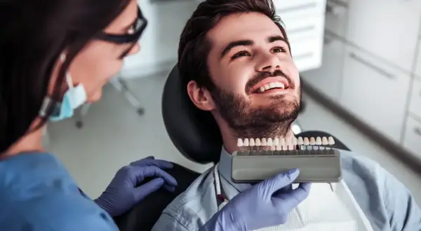 Dentystka dobiera odcień licówek kompozytowych dla uśmiechniętego pacjenta.