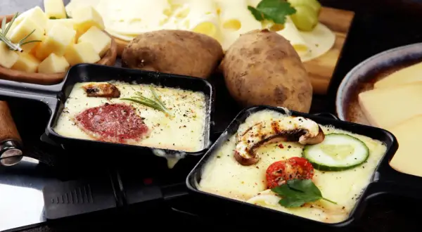 Schmelzender Raclette-Käse mit Salami und Pilzen, dazu Kartoffeln und ein Glas Wein. Perfekt für einen gemütlichen Abend.