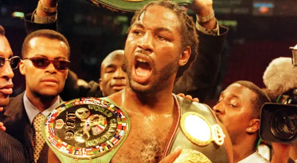 Lennox Lewis, triumphant, wears multiple championship belts, a symbol of his boxing dominance.