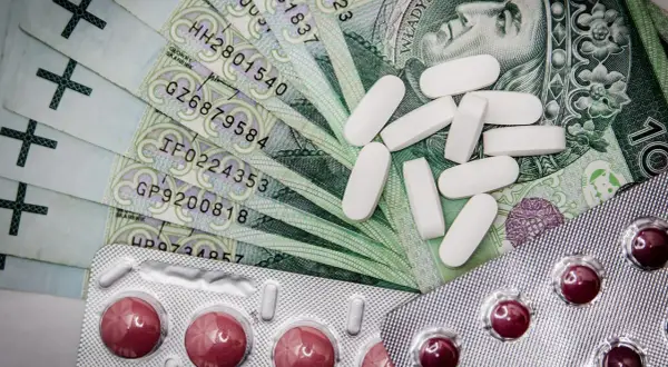Polskie banknoty, białe i czerwone tabletki w blistrach.