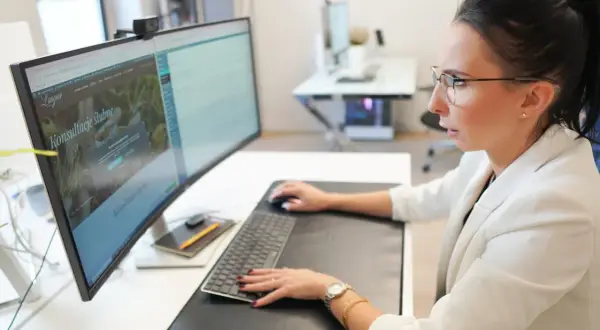 Kobieta w okularach pracuje przy komputerze, na ekranie której widoczna jest darmowa strona internetowa z ofertą konsultacji ślubnych.