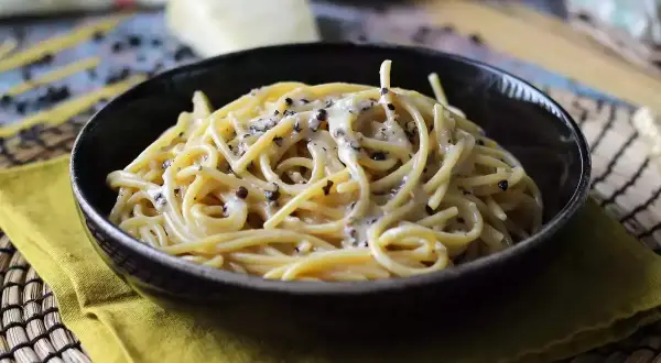 Miseczka spaghetti cacio e pepe, z kremowym sosem serowym i pieprzem, na żółtej serwetce.