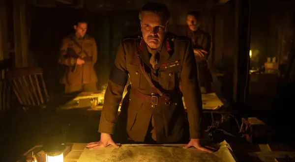 Ein General studiert im Schein einer Lampe eine Karte. Die besetzung von 1917 (film) zeigt ihn mit zwei Offizieren im Hintergrund.
