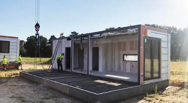 Budowa domu modułowego w toku. Dźwig podnosi element konstrukcji. Pozwolenie na budowę zostało uzyskane, prace postępują.