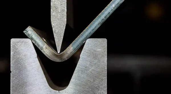 Metal sheet being bent by a press brake tool.