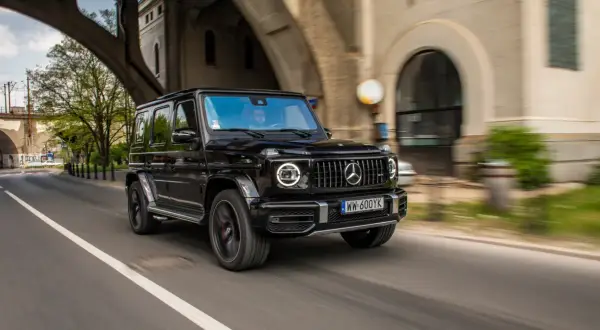 Czarny Mercedes G63 z okrągłymi światłami LED pędzi pod wiaduktem.