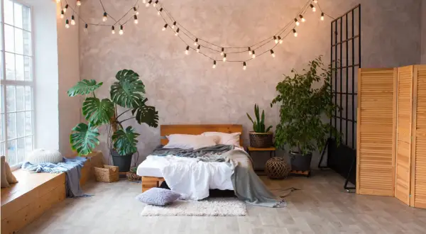 Przytulna sypialnia boho loft z łóżkiem, roślinami i girlandą świetlną.