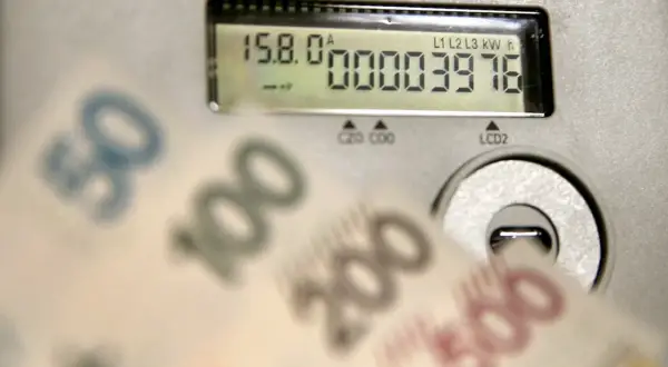 Liczniki energii PGE pokazują zużycie, a przed nimi banknoty 50, 100, 200, 500 zł. Opłata sieciowa PGE może być wysoka.