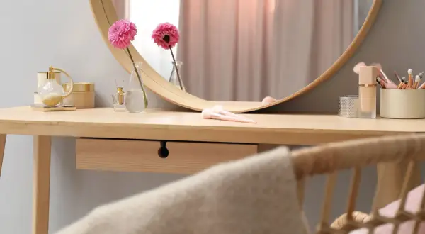 Eleganckie krzesło do toaletki z rattanowym oparciem, obok drewnianego blatu z kosmetykami i kwiatami.