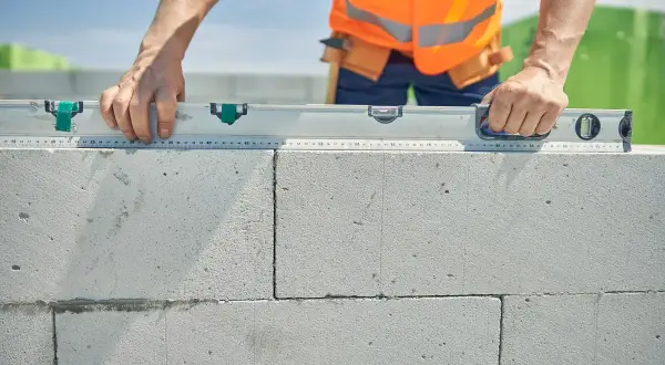 Budowniczy sprawdza poziom ścianki z bloczków. Dokładne wymierzenie ile suporexu na m2 jest kluczowe dla stabilności konstrukcji.