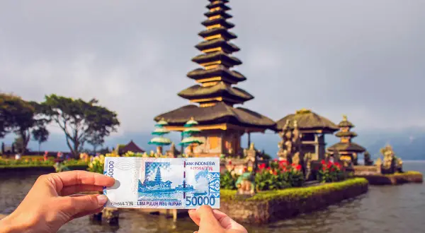 Ręka trzyma banknot 50 000 rupii indonezyjskich na tle świątyni na wodzie na Bali.