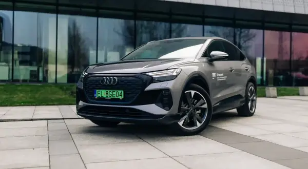 Szary Audi Q4 elektryk z zieloną tablicą rejestracyjną stoi przed nowoczesnym budynkiem.
