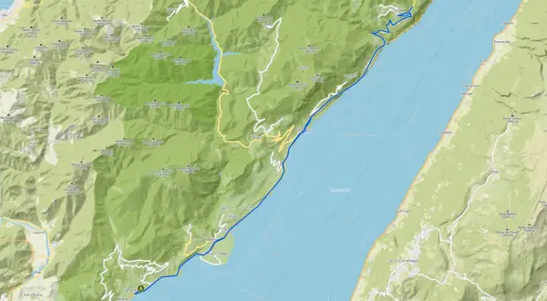 Il lungolago di Gardone Riviera si estende lungo il Lago di Garda, con montagne verdi che si affacciano sull'acqua.
