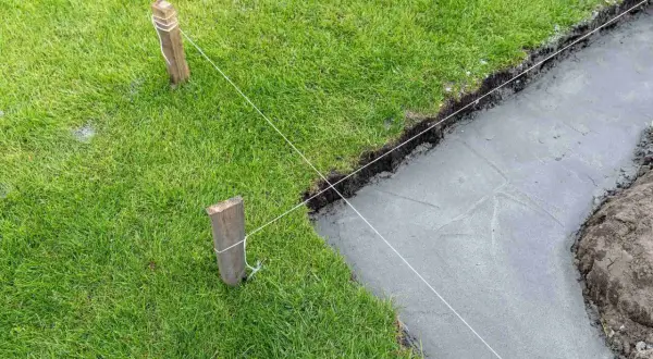 Wyznaczanie fundamentów domu. Naciągnięte sznurki wyznaczają linię wykopu pod uziemienie domu, obok świeżo wylany beton.