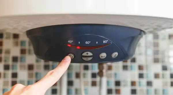 Palec naciska przycisk na bojlerze, zastanawiając się, czy bojler elektryczny pobiera dużo prądu. Wyświetlacz pokazuje temperaturę.