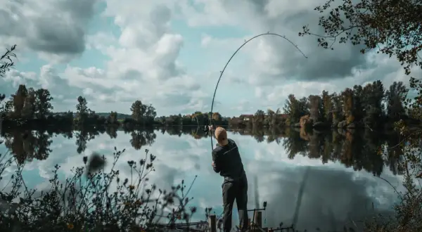 Wędkarz łowi na ciężki spinning z opadu w głębokich rynnach odrzańskich. Wędka wygięta w łuk, woda spokojna, odbija chmury.