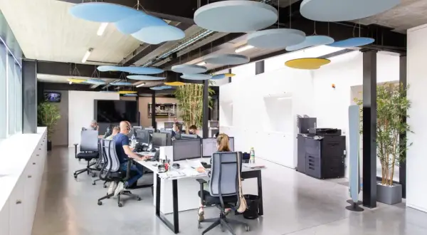 Bureau moderne avec employés concentrés, malgré le bruit ambiant. Des panneaux acoustiques colorés au plafond réduisent le bruit au travail.