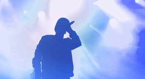Silhouette di un rapper con microfono, luci blu e bianche sullo sfondo. Le origini di Tony Boy.