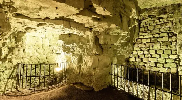 Intérieur des boves d'Arras, un réseau de galeries souterraines aux murs de pierre brute et de briques, éclairées par une lumière jaune.