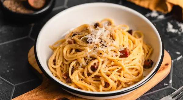 Ein Teller mit authentischer Spaghetti Carbonara, garniert mit Pecorino und schwarzem Pfeffer.