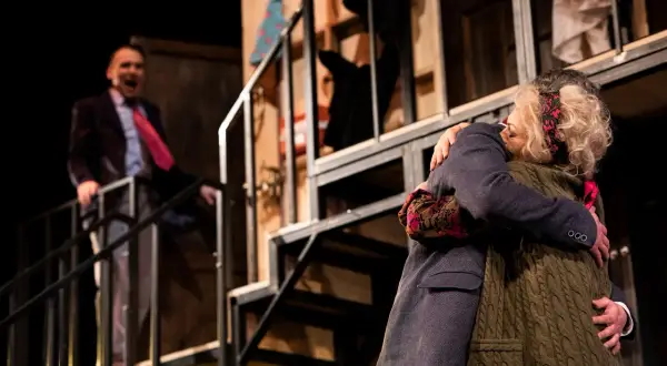 Na scenie Teatru Osterwy wzruszające objęcie dwóch postaci. W tle mężczyzna w garniturze krzyczy, co nie widać.