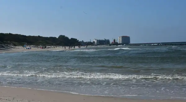Słoneczny dzień nad Bałtykiem, plaża pełna ludzi, a w oddali widać miasto u ujścia Wieprzy.