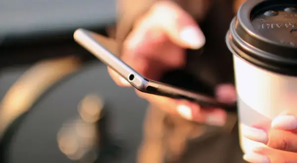 Kobieta trzyma telefon i kubek kawy, szukając informacji, jak się doładowuje Play.