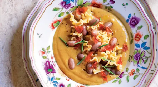 Pasta e Fagioli with ruffled pasta, beans, and crispy pancetta on a floral plate.