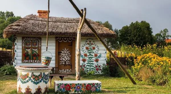 Tradycyjna chata z malowanymi kwiatami, studnia i kwitnące żółte kwiaty. Wygląda jak najpiękniejsza wieś w Polsce.
