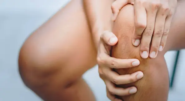 Hände umfassen ein schmerzendes Knie. Was tun bei Knieschmerzen?