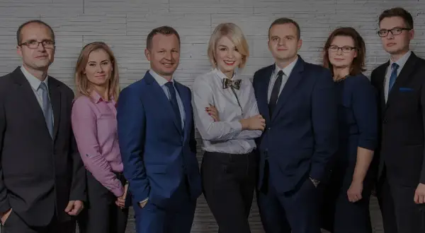 Grupa prawników w eleganckich strojach pozuje do zdjęcia na tle ściany z cegły.