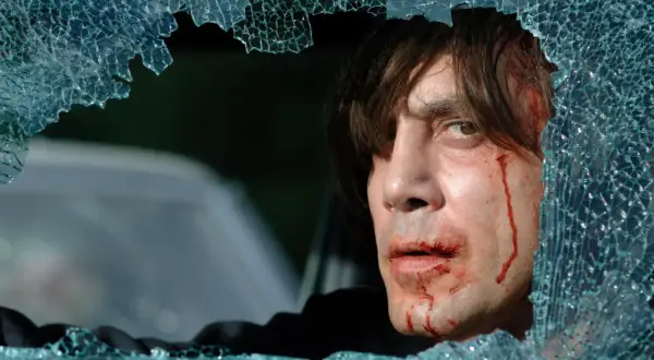 Javier Bardem w jednym z mrocznych filmów, z krwawiącą twarzą, patrzy przez pękniętą szybę.
