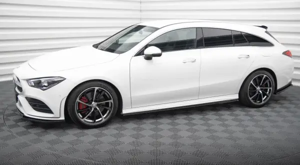 Biały Mercedes CLA shooting brake z czarnymi felgami i czerwonymi zaciskami hamulcowymi stoi na szarej, kratkowanej podłodze.