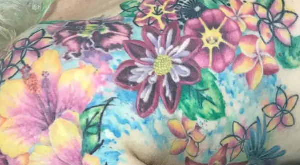 Buntes Blumen-Tattoo, das Lebensfreude nach einer Krebserkrankung symbolisiert. Hibiskus und andere tropische Blüten in leuchtenden Farben.