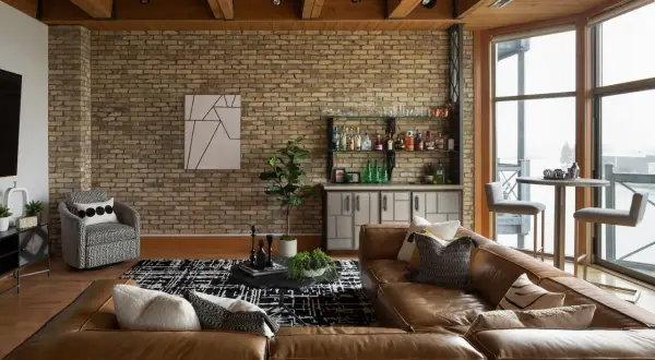 A rustic modern living room with exposed brick, wood beams, a leather sofa, and a home bar.