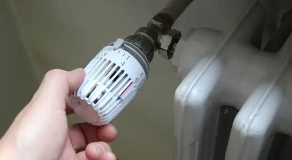 Mano che regola la manopola del termosifone, scegliendo tra senso orario o antiorario per la temperatura desiderata.