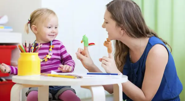 Radosna opieka nad zdrowym dzieckiem. Mama bawi się z córką pacynkami na palcach, rozwijając jej wyobraźnię.